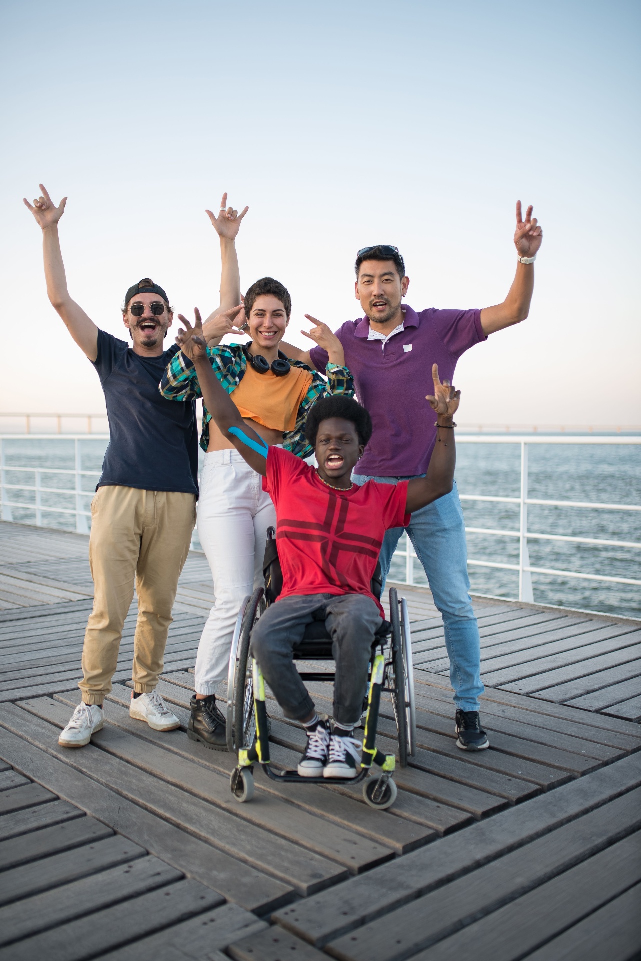 A group of friends, one using a wheelchair, celebrating together on a waterfront pier